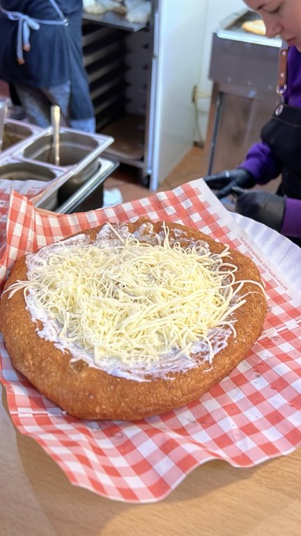 The classic lángos being prepared with sour cream and grated cheese