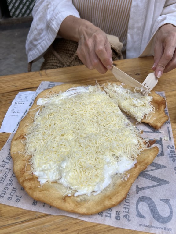 Cutting a cheese and sour cream langos at an outdoor table